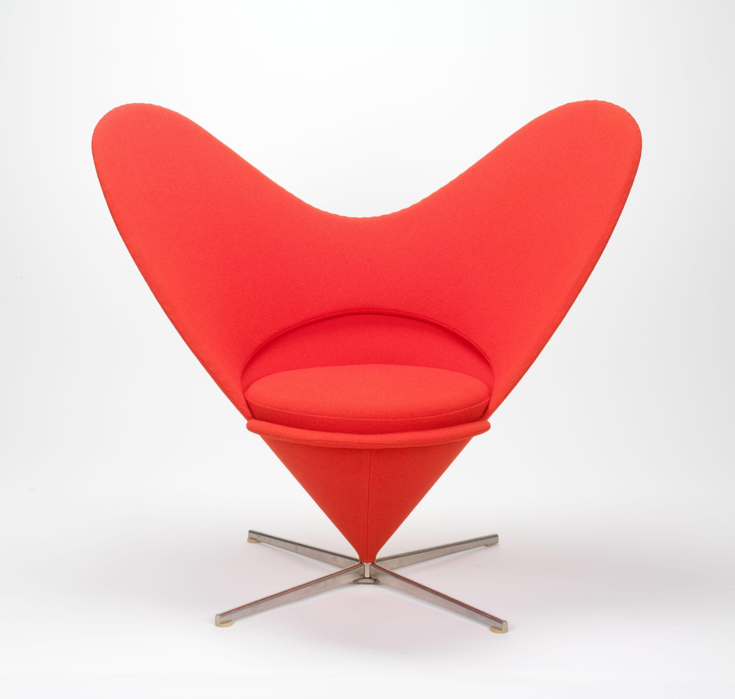 A bold red, heart-shaped chair with sweeping, curved wings and a metallic cross-shaped base.