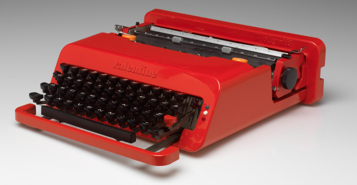 A bright red portable typewriter designed by Ettore Sottsass, Jr., and Perry A. King, manufactured by Olivetti in 1969. The compact typewriter, known as the Valentine, has a sleek, modern design with black keys and is intended to be lightweight and portable.