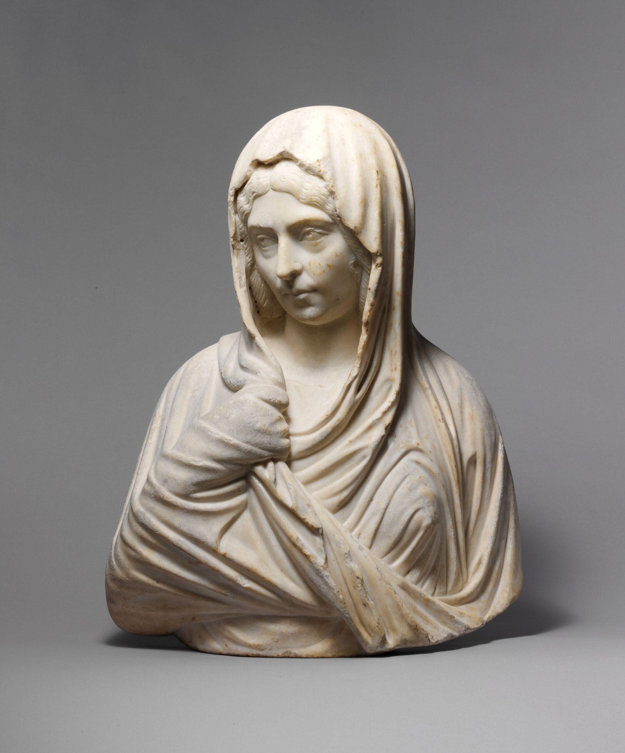 A marble portrait bust of a woman from ancient Rome, dated circa 193–211 CE. The sculpture depicts a woman draped in a finely detailed garment with a veil covering her head. Her expression is contemplative, and the craftsmanship highlights the folds of the fabric and the texture of her hair.